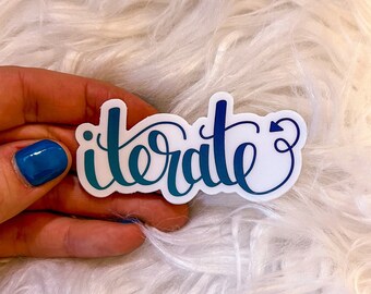 May include: A white sticker with the word "iterate" written in blue and teal cursive lettering with a small arrow at the end of the word.