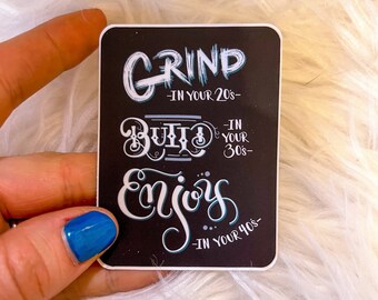 May include: Black and white sticker with the text "Grind in your 20s, Build in your 30s, Enjoy in your 40s".