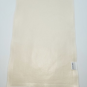 Puede incluir: Paño rectangular blanquecino con superficie texturizada y bordes cosidos. Una pequeña etiqueta blanca con el texto "LISS & LANDT" está adherida en la esquina inferior derecha. El paño parece estar hecho de fibra natural.