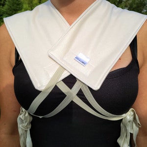 May include: A white fabric collar with a white label that says "LESS & LAID", worn over a black top with beige straps.