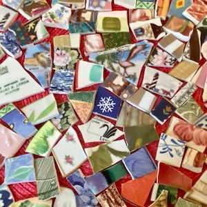 May include: A collection of assorted ceramic shards featuring various patterns, colors, and illustrations including a flamingo, a lighthouse, a snowflake, and a swan. The fragments display diverse floral, geometric, and landscape designs.