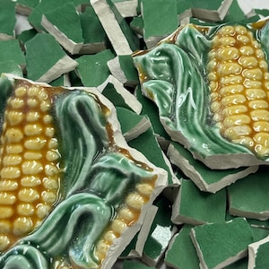 May include: Broken ceramic tiles featuring a corn cob design. The tiles have a glossy finish with yellow, brown, and green colors. The image shows a pile of broken pieces, suggesting a mosaic or decorative project.
