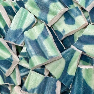 May include: A collection of broken ceramic tiles with a mix of green and blue patterns. The tiles have a rough, textured surface and a light-colored edge. The color palette includes shades of teal, seafoam green, and navy blue.