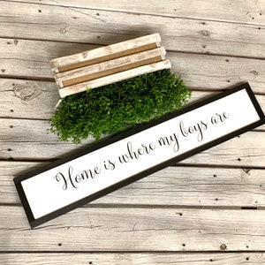 May include: A black framed sign with white background and the text "Home is where my boys are" in black cursive font. The sign is on a white wood background.