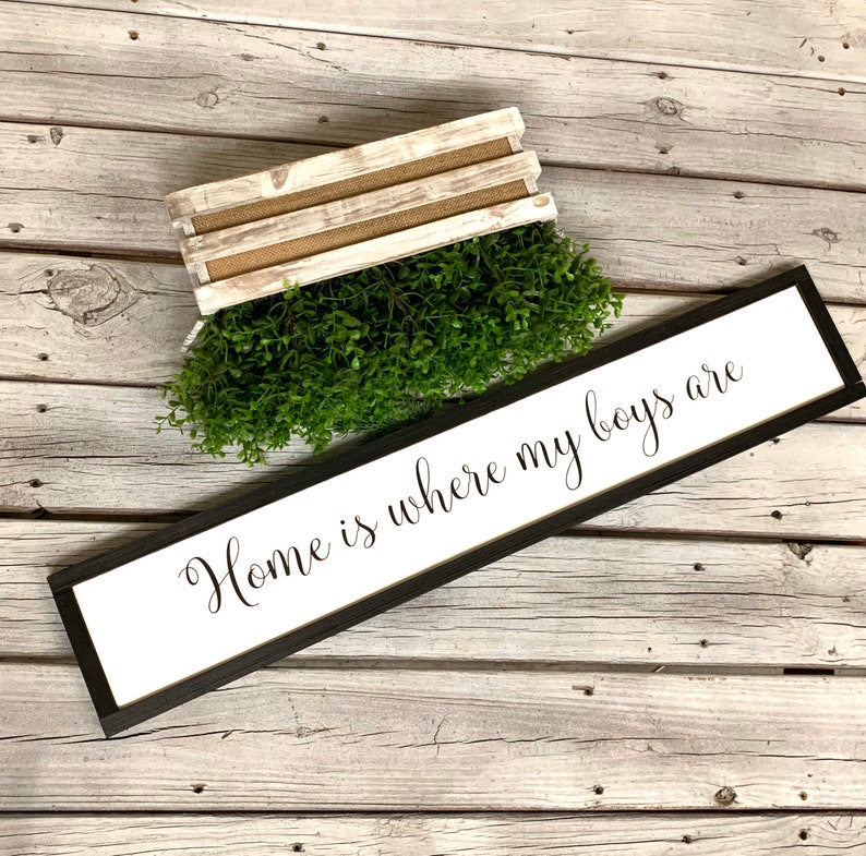 May include: A black framed sign with white background and the text "Home is where my boys are" in black cursive font. The sign is on a white wood background.
