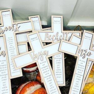 May include: A collection of wooden crosses with personalized names and the text "Be strong and courageous. Do not be afraid; do not be discouraged, for the Lord your God will be with you wherever you go. Joshua 1:9" printed on them.
