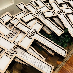 May include: A basket filled with wooden crosses, each with a different name and a Bible verse. The crosses are painted in a light wood color and have a clear acrylic insert for a photo.