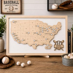 May include: A framed wooden map of the United States featuring engraved state borders and small baseball icons marking various stadium locations. A wooden plaque in the bottom right corner displays the text The Bridges Stadium Tour.