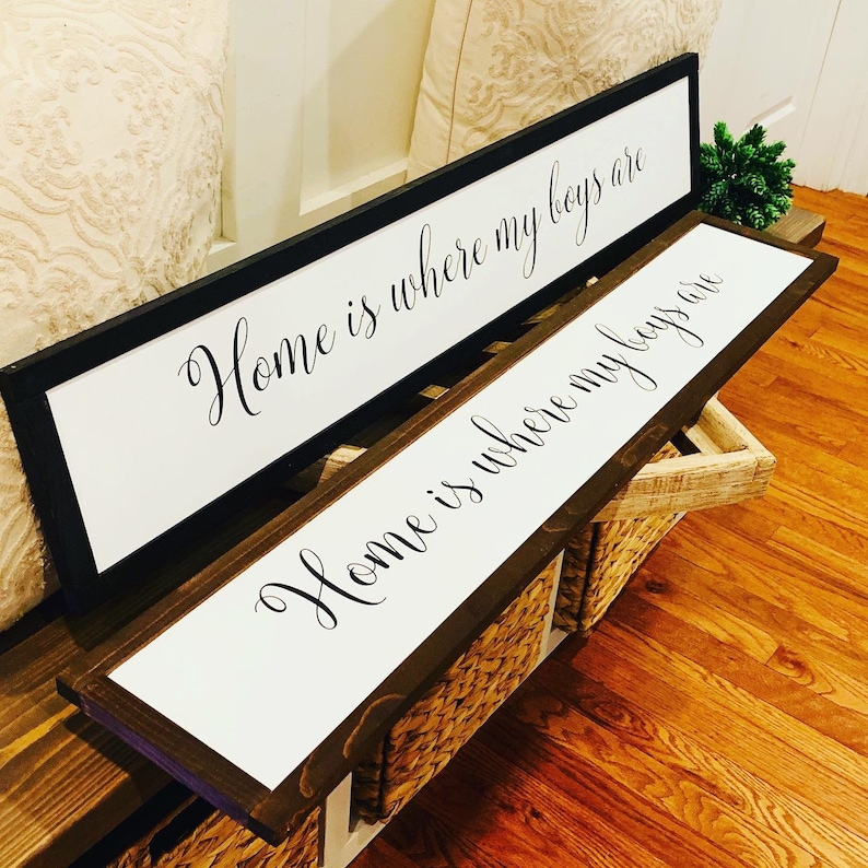 May include: Two wooden signs with white backgrounds and black calligraphy. The top sign reads "Home is where my boys are" and the bottom sign reads "Home is where my boys are".