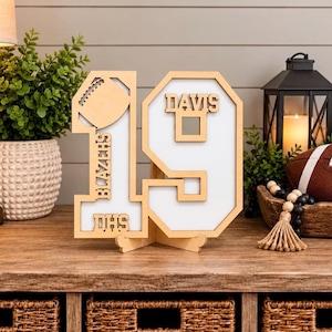 May include: A freestanding wooden number 19 sign with a white background. The number 1 features a football cutout, the text BLAZERS, and DHS. The number 9 features the name DAVIS. The sign is constructed from light-colored wood with a layered design.