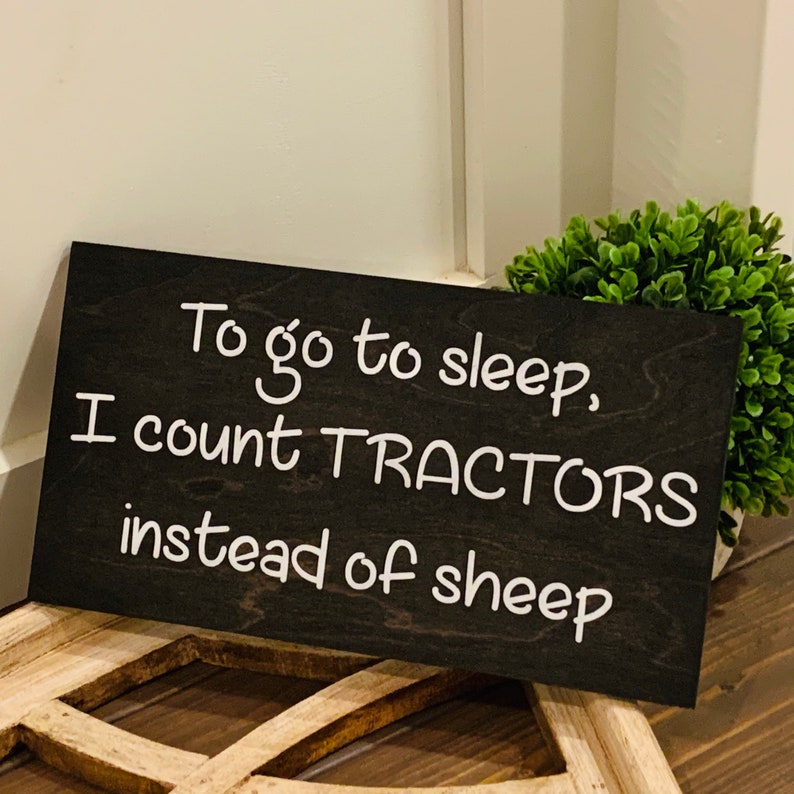 Peut inclure: Une pancarte en bois noir avec du texte blanc qui dit "Pour aller dormir, je compte des TRACTEURS au lieu des moutons."