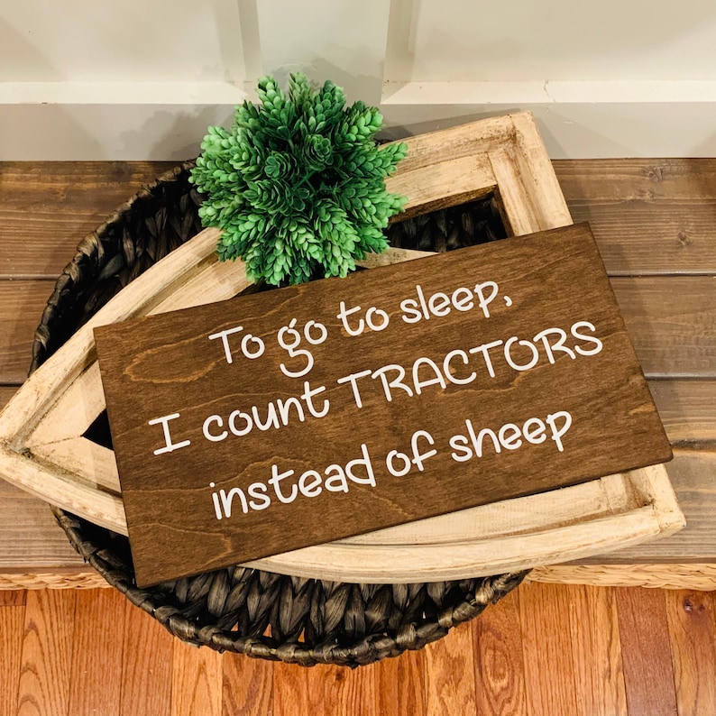 Peut inclure: Une pancarte en bois brun avec du texte blanc qui dit "Pour aller dormir, je compte des TRACTEURS au lieu des moutons".
