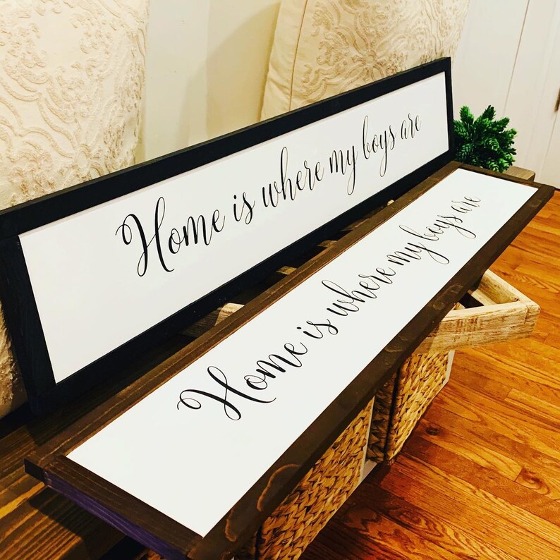 May include: Two wooden framed signs with white backgrounds and black calligraphy. The top sign reads "Home is where my boys are". The bottom sign reads "Home is where my boys are".