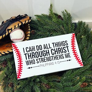 May include: White wooden sign with red stitching around the edges, resembling a baseball. The sign reads "I can do all things through Christ who strengthens me - Philippians 4:13".