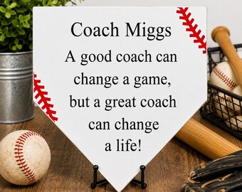 May include: A white home plate-shaped sign with red baseball stitching graphics on the corners. The text reads: Coach Miggs, A good coach can change a game, but a great coach can change a life! The sign is displayed on a small black metal stand.