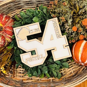 May include: A wooden cutout of the number 54 with a white center, featuring the text "PIONEERS" vertically on the right side, "POSTILL" horizontally at the bottom, and "CHS" with a football graphic in the upper left corner of the number 5.