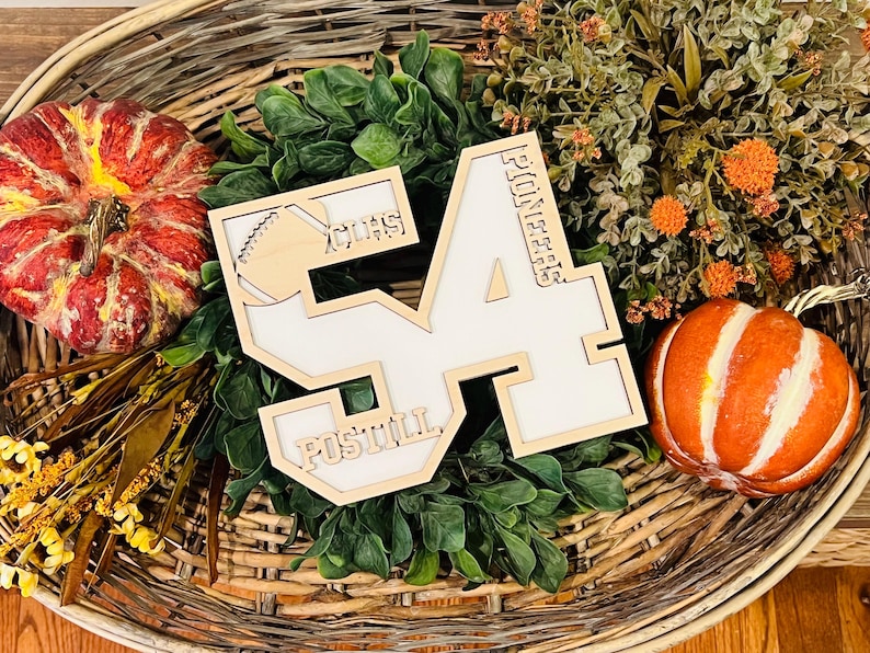 May include: A wooden cutout of the number 54 with a white center, featuring the text "PIONEERS" vertically on the right side, "POSTILL" horizontally at the bottom, and "CHS" with a football graphic in the upper left corner of the number 5.