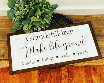 May include: A white wooden sign with a brown frame reads "Grandchildren make life grand" with the names Amelia, Elliott, Sadie, and Jacob listed below.
