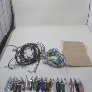 May include: A collection of hexagonal crystal point pendants in various colors, including black, white, green, blue, and pink. The set includes multiple black and multicolored cord necklaces with silver-tone clasps and a small beige burlap pouch.