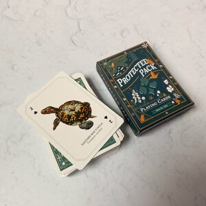 May include: A deck of playing cards with a box featuring a nature-themed design. The cards show an illustration of an Eastern Box Turtle. The box reads "PROTECTED PACK PLAYING CARDS PGH, PA, USA."
