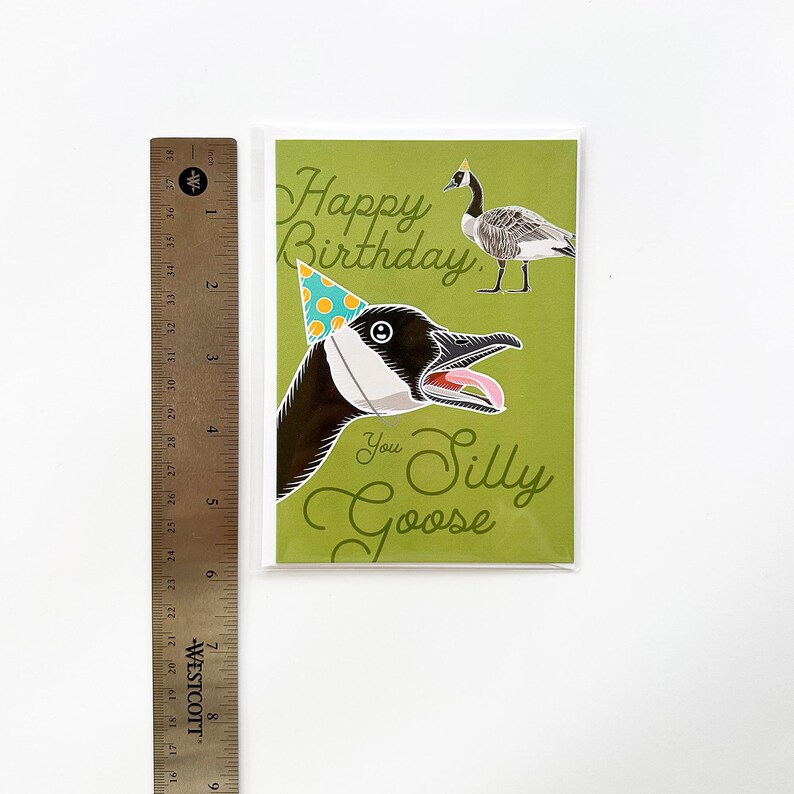Silly goose birthday card in protective plastic sleeve displayed head-on with metal ruler for size reference. Green funny birthday card measures 5.83 inches tall.