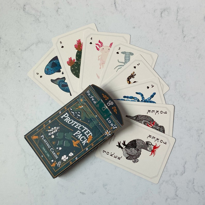 May include: A deck of "Protected Pack" playing cards with a teal and gold box. The cards feature illustrations of various creatures and plants. Some cards are fanned out, displaying the card faces. The box reads "PLAYING CARDS" and "PROTECTED PACK".