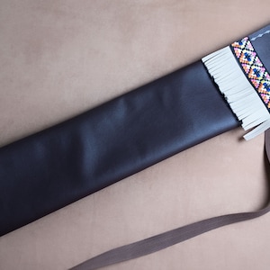 May include: A brown leather case with a white fringe and colourful geometric pattern. The case has a strap and a button closure.