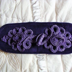 May include: A purple velvet fabric with two decorative purple knotted fabric embellishments.