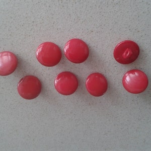 May include: Eight red plastic buttons with a single hole in the centre. One button has a metal shank on the back.