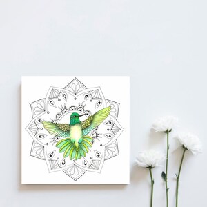 May include: A green and yellow hummingbird with outstretched wings is flying in the center of a black and white mandala. The mandala is a circular design with intricate patterns.