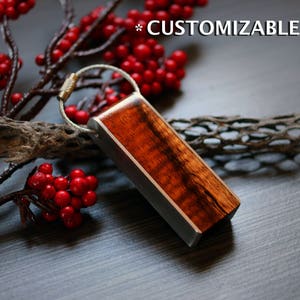 May include: A rectangular wooden keychain with a silver metal frame. The wood has a rich, reddish-brown grain. The keychain is attached to a silver metal loop. The word "CUSTOMIZABLE" is above the keychain.