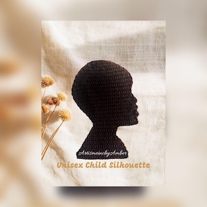 Op de afbeelding: Een donkerbruin gehaakt silhouet van een kinderprofiel. De tekst "ArtismeincbyAmber" en "Unisex Child Silhouette" staan eronder. De afbeelding is geplaatst tegen een neutrale achtergrond met gedroogde bloemen.