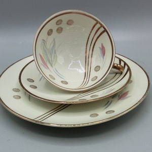 Peut inclure: Un ensemble de tasse et soucoupe en porcelaine blanche avec une bordure dorée et un motif floral. La tasse et la soucoupe présentent un motif délicat de points dorés et de fleurs stylisées dans des tons de rose, bleu et vert.