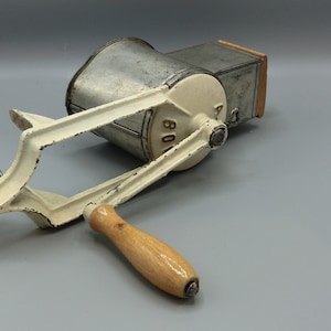 Peut inclure: Un ancien hachoir à aliments en métal blanc cassé et argenté, avec une poignée en bois. Il est équipé d'une pince pour le fixer. Le chiffre "80" est visible. Cet appareil est probablement utilisé pour hacher de la viande ou des légumes. Mesures en centimètres.