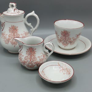 Könnte beinhalten: Ein weißes Teeservice mit rotem Blumenmuster. Das Set beinhaltet eine Teekanne, eine Milchkännchen, eine Tasse, eine Untertasse und eine kleine Schale.