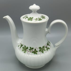 Op de afbeelding: Witte porseleinen theepot met een groen wijnstokontwerp. De theepot heeft een deksel en een handvat.