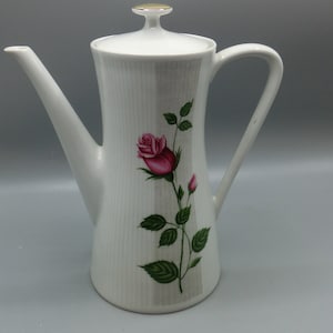 Könnte beinhalten: Weiße Kaffeekanne aus Keramik mit goldfarbenem Rand am Deckel und einem Design mit einer einzelnen rosa Rose mit grünen Blättern.