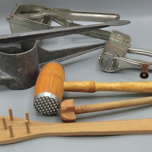Può includere: Una collezione di utensili da cucina vintage, tra cui uno spremiaglio, un batticarne, una grattugia e un server per pasta in legno. Gli utensili sono realizzati in metallo e legno, con un aspetto rustico.