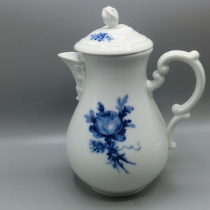 Könnte beinhalten: Weiße Porzellan-Milchkanne mit blauem Blumendesign und Deckel. Die Kanne hat einen runden Körper und einen Henkel mit einem dekorativen Schnörkeldesign.