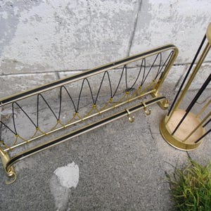 Può includere: Un set vintage di attaccapanni e portaombrelli in metallo dorato. L'attaccapanni ha un design rettangolare con dettagli neri e ganci. Il portaombrelli è cilindrico con barre verticali nere. Entrambi i pezzi hanno un'estetica moderna della metà del secolo.