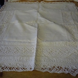 Può includere: Una tovaglia rettangolare bianca con intricati dettagli in pizzo. I bordi presentano un bordo in pizzo smerlato e il centro ha una sezione piegata liscia. Il design in pizzo include motivi floreali e geometrici, creando un aspetto delicato ed elegante.