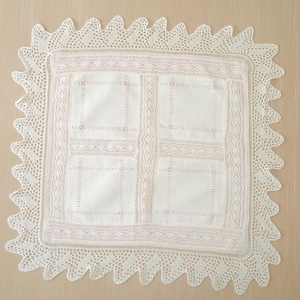 May include: A white crocheted doily with a delicate lace border and a pink embroidered design in the center.