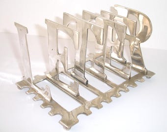 May include: Silver letter holder with the word "LETTER" spelled out in the design. The holder has a decorative base with a scalloped edge.