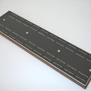 May include: A rectangular cribbage board with a dark gray playing surface and numerous small holes for peg placement. The board has a wooden frame with a silver border and is secured with silver screws.