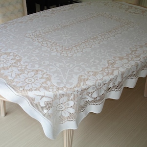 May include: White oval tablecloth with a delicate floral lace pattern. The tablecloth is made of a lightweight material and has a scalloped edge.