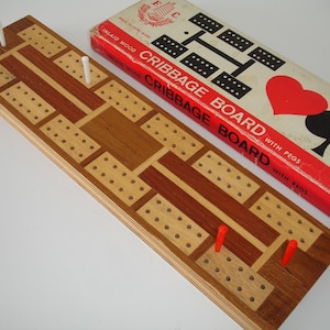 May include: A wooden cribbage board with pegs. The board is made of inlaid wood and has a red and brown design. The box is red with black and white playing card suits.