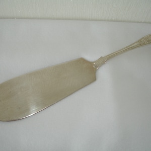 May include: A silver cake server with an ornate handle. The blade is smooth and polished.