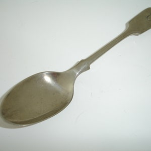 May include: A silver spoon with a rounded bowl and a long, slender handle. The handle has a simple, rounded design and is engraved with the letter "H".