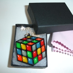 May include: A colorful Rubik's Cube pendant necklace with a silver chain, presented in a black gift box. The cube features red, blue, green, yellow, and gray squares. A pink cleaning cloth is also included.