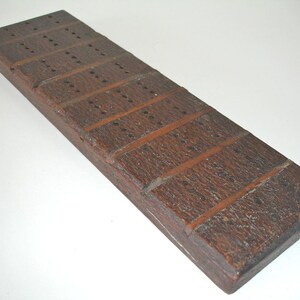 May include: A dark brown wooden cribbage board. The board is rectangular with rows of small holes for pegs and carved lines dividing the sections. A traditional board game accessory, approximately 30 cm long.